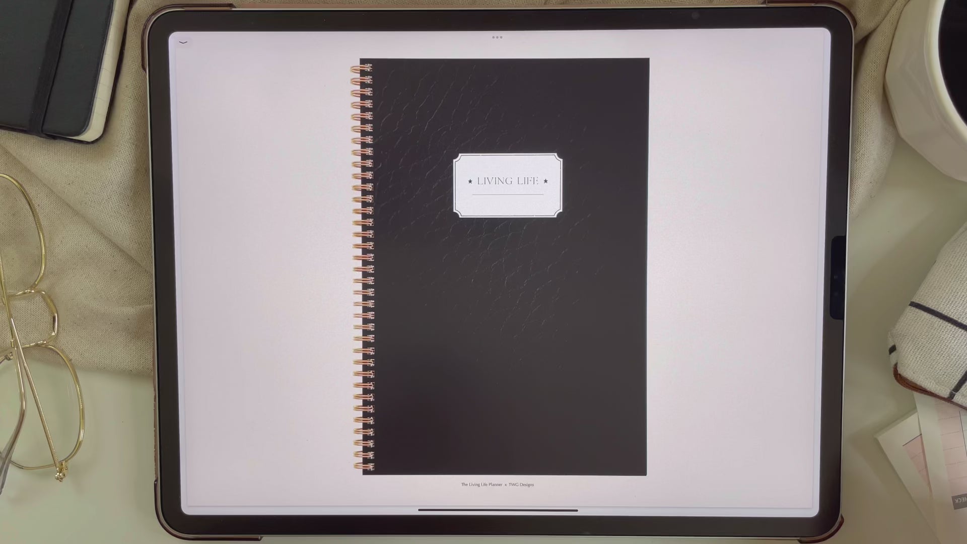 Black cover of digital planner on iPad with gold spiral binding, surrounded by minimal props.